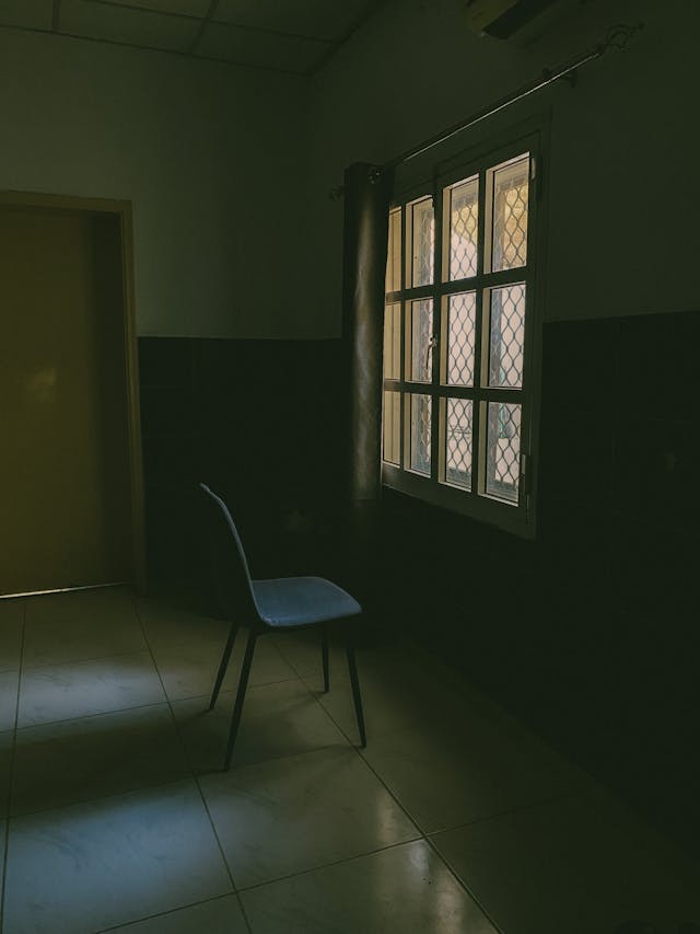 Een rustige, lege kamer met een enkele stoel bij het raam, ingetogen daglicht
